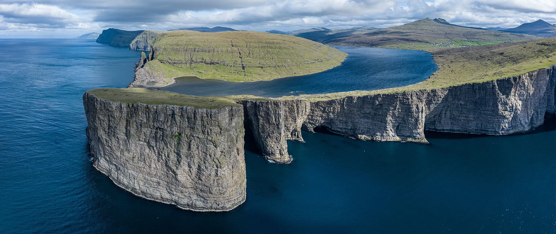 The lake and sea are both eerily calm with matching shades of blue. The subtle criss-crossing waves appear in a different direction in the lake compared to the sea, and the lake is surrounded by green-tinged land atop the cliffs, creating the impression <br />that the lake has been badly photoshopped into place.