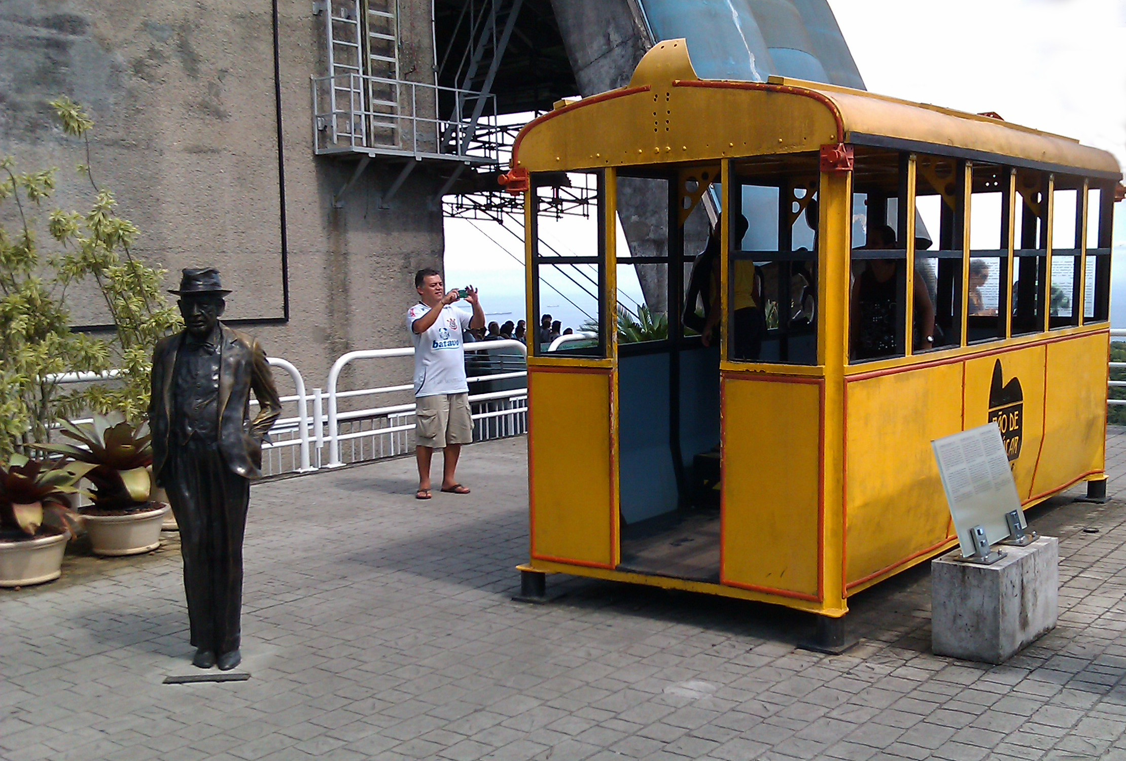 A yellow (old) cable car beside a statue of a man wearing a hat. A yellow (old) cable car beside a statue of a man wearing a hat.